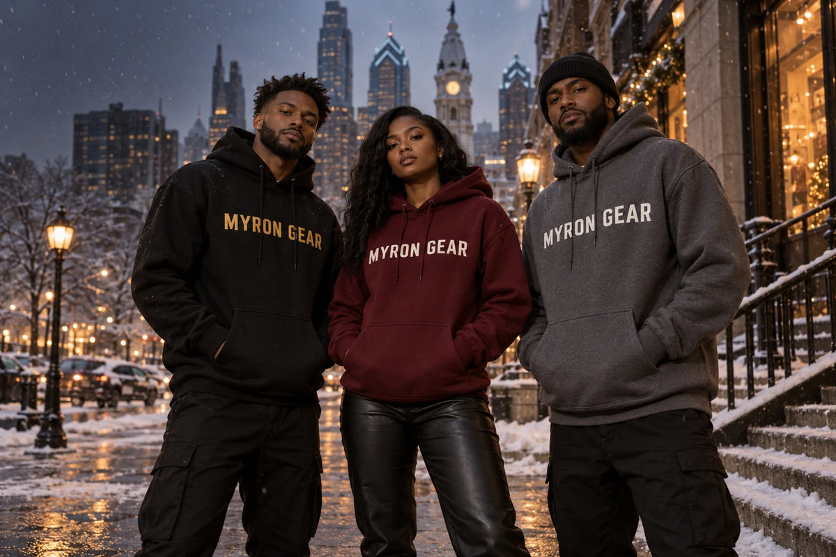 Two Black men and one Black woman wearing black, burgundy and charcoal MYRON GEAR hoodies on a Philadelphia street